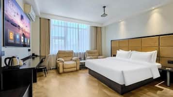 A hotel room with a large bed, a desk with a chair, a sofa, and a TV mounted on the wall.