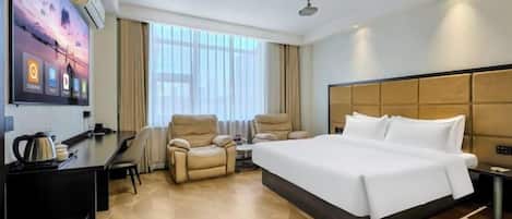 A hotel room with a large bed, a desk with a chair, a sofa, and a TV mounted on the wall.