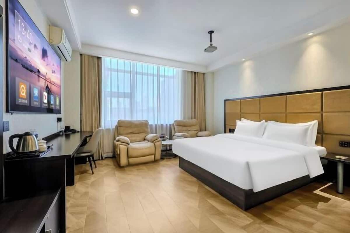A hotel room with a large bed, a desk with a kettle, a TV, and a window with curtains.