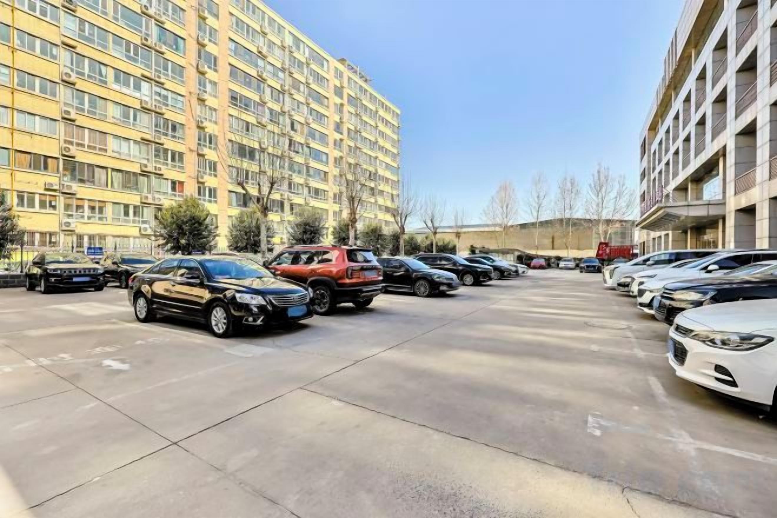 A parking lot with multiple cars parked in front of a multi-story building.