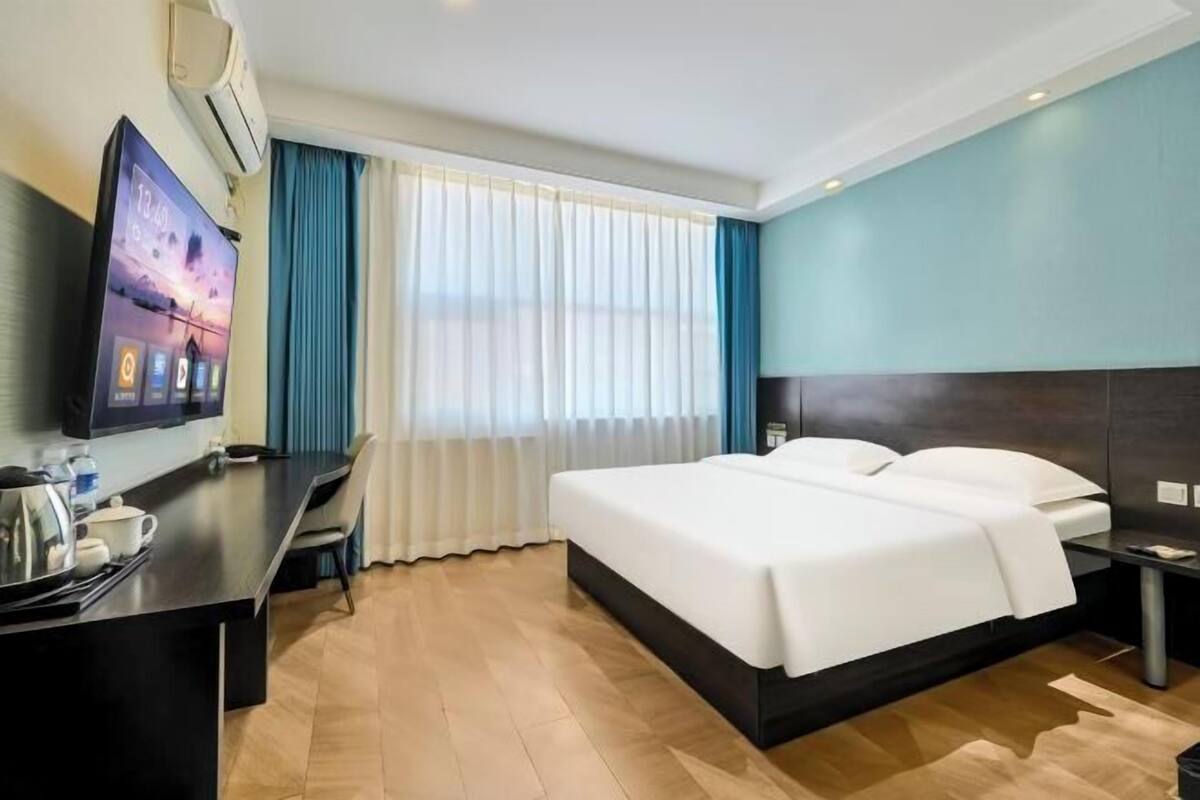 A hotel room with a bed, a desk with a computer, a TV, and a window with curtains.