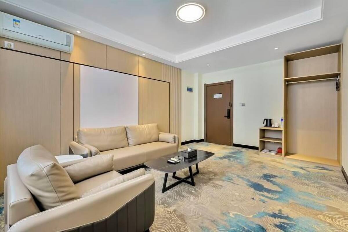 A hotel room with a beige sofa, a small coffee table, a large mirror, and a wardrobe.