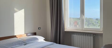 Una habitación de hotel con cama, ventana con vistas, radiador y una silla.