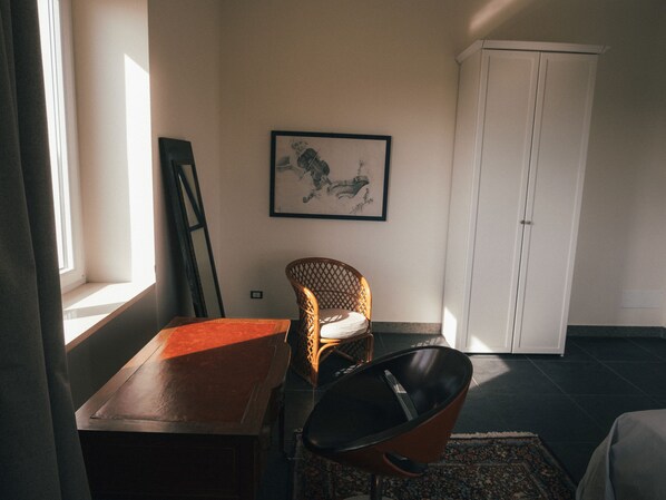 A room with a wicker chair, a table, a cabinet, and a framed picture on the wall.