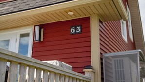 A house with a red exterior, a white porch, and a number '63' on the front. - Twillingate Little Suite w/ Ocean & Garden View (Twillingate)