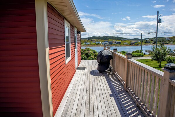 A red building with a wooden deck and a view of a lake. - Twillingate Little Suite w/ Ocean & Garden View (Twillingate)