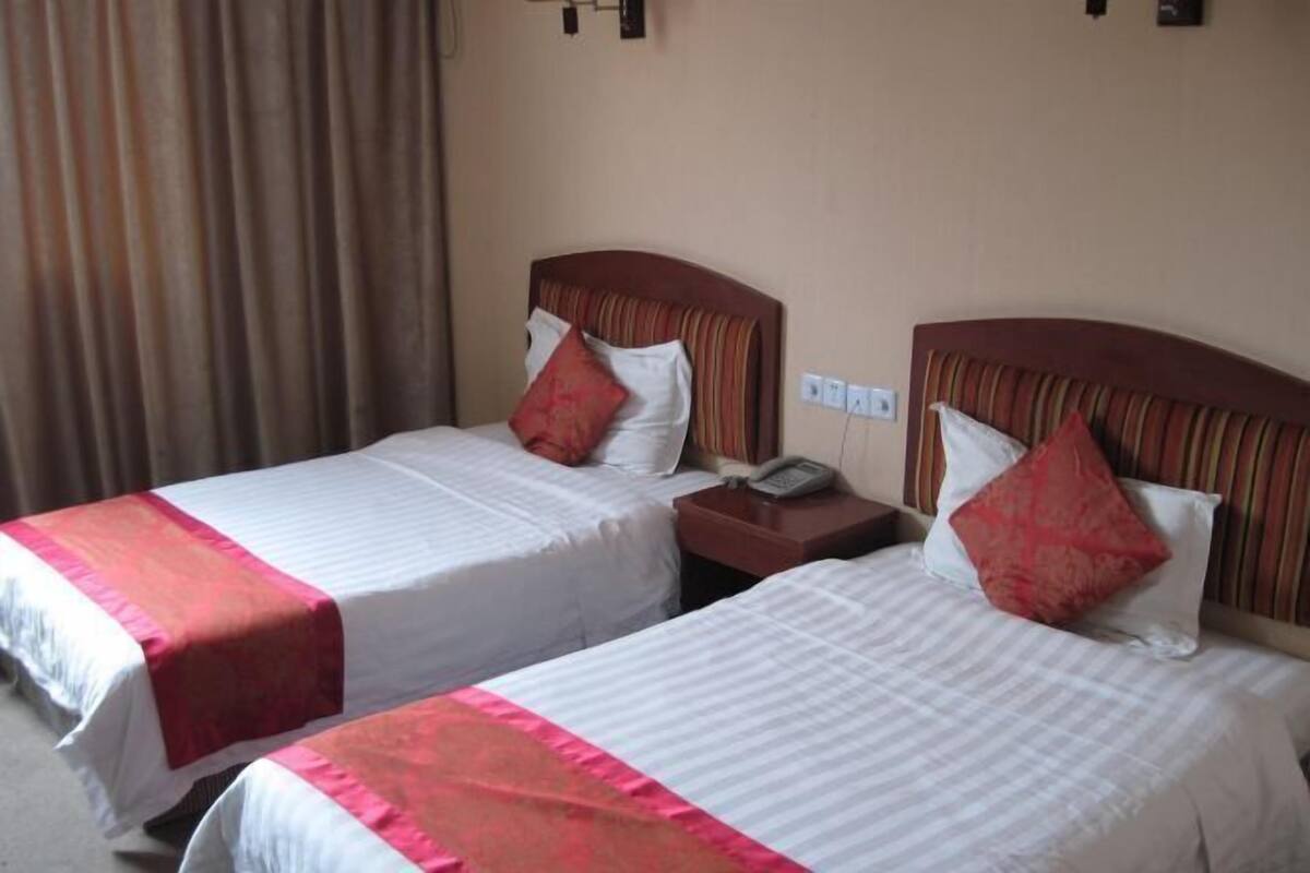 Une chambre d’hôtel avec deux lits, chacun doté d’une tête de lit, d’une table de chevet avec un téléphone et d’un rideau sur le côté gauche.