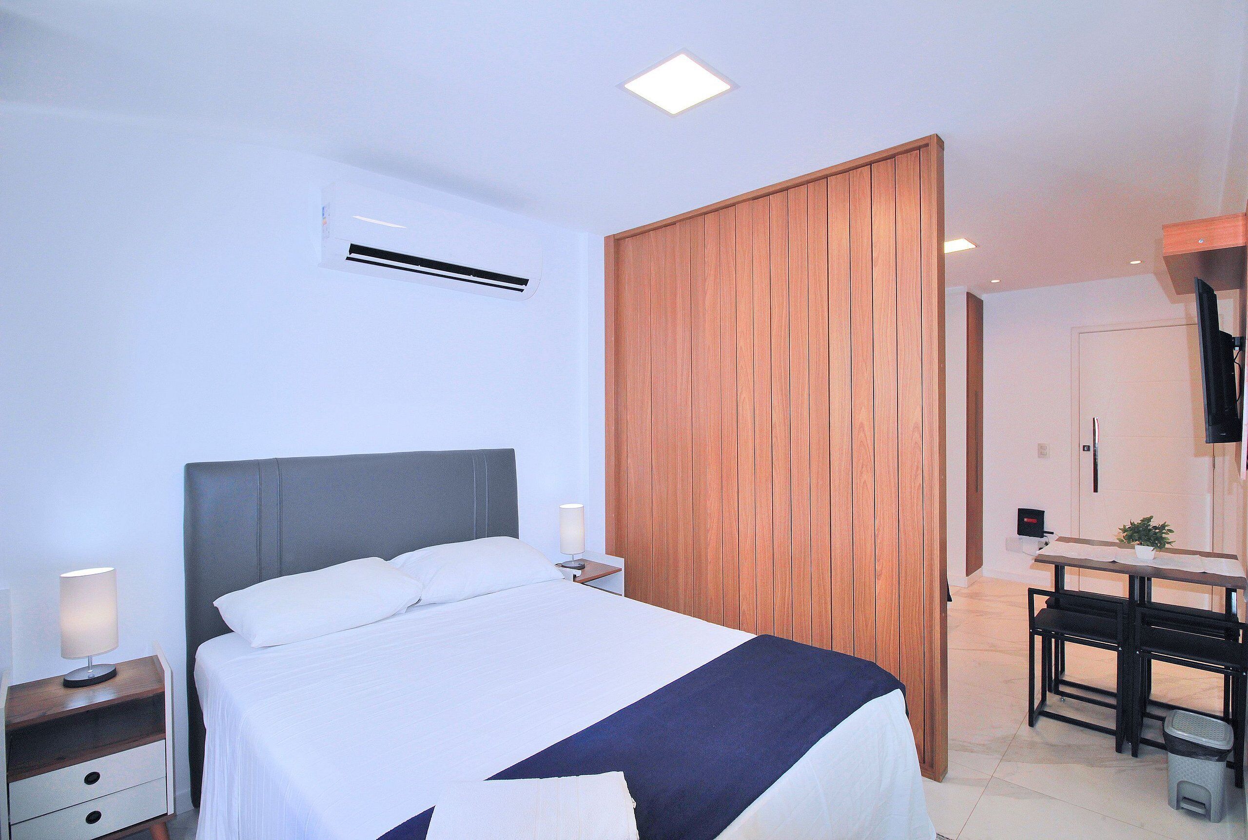 A modern hotel room with a bed, bedside tables, a desk, and a wardrobe.