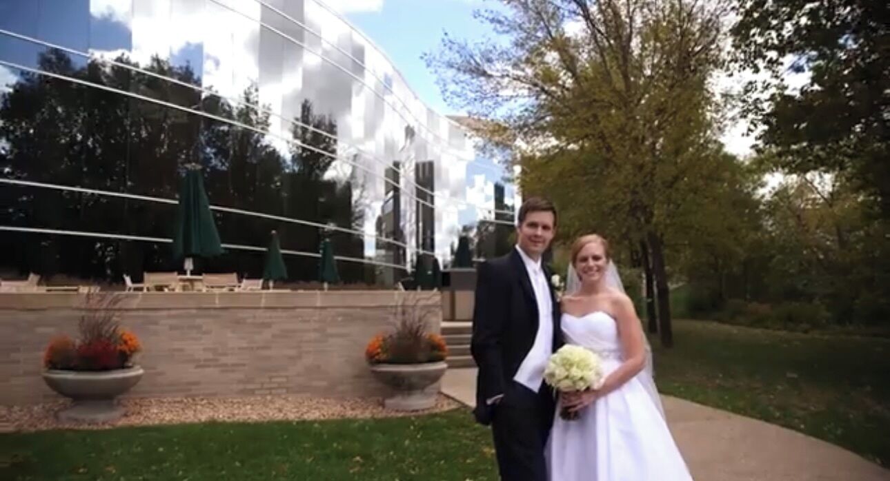 A couple in wedding attire standing in front of a building with a glass facade and outdoor seating.