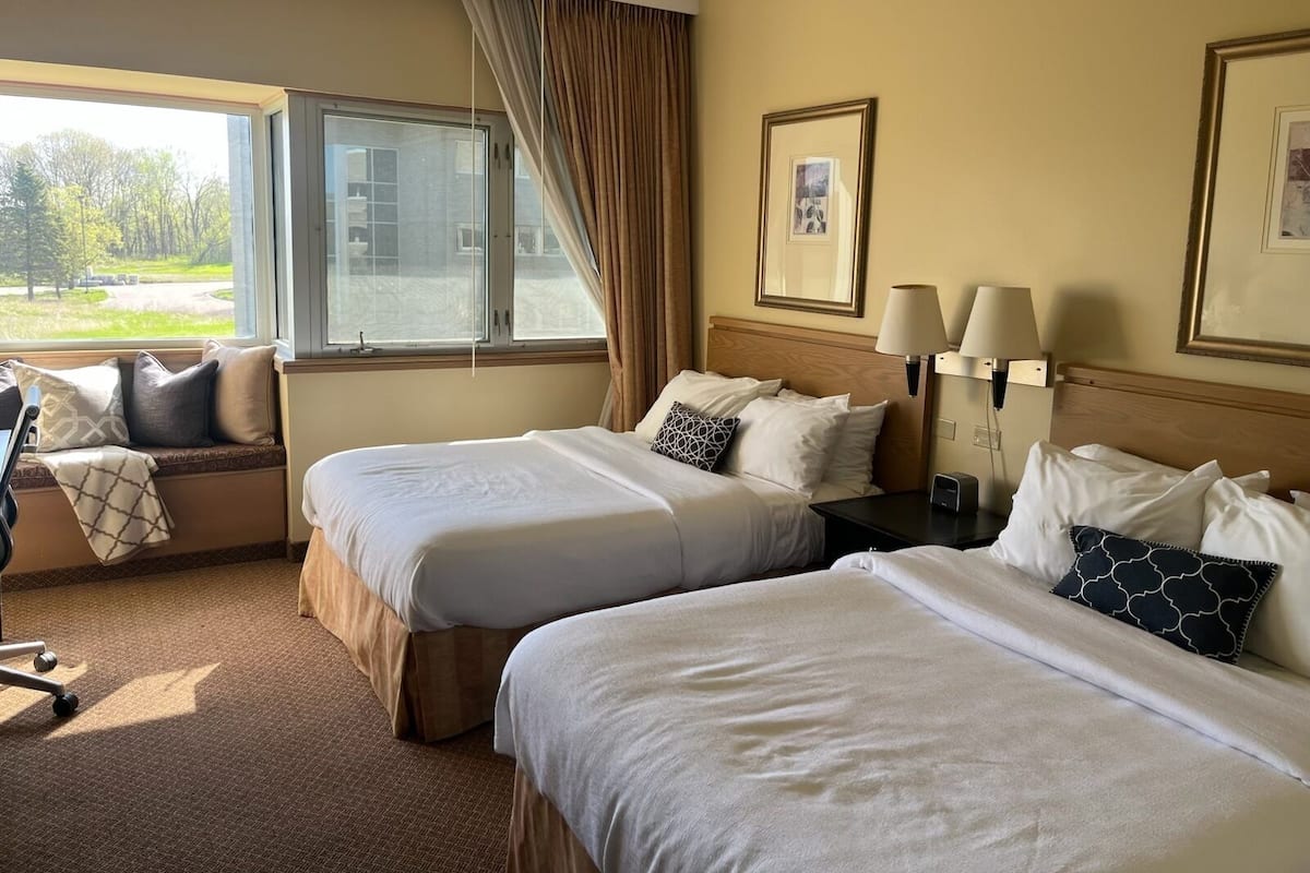 A hotel room with two beds, a window with a view of a golf course, a desk with a chair, and two bedside lamps.