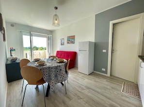 Un comedor con una mesa dispuesta para cuatro, un sofá rojo, un refrigerador blanco y una puerta que da a un balcón.