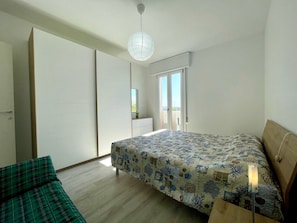 Un dormitorio con cama, una silla verde, un armario y una puerta corredera que da a un balcón.