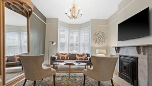 A living room with a fireplace, a television mounted on the wall, and a large window with blinds. - 4 Bed 1.5 Bath, 3 Story Townhouse, Free Parking (Milwaukee)