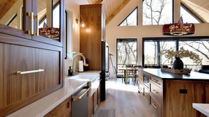 A modern kitchen with wooden cabinets, a large window, and a view of trees. - Modern Cabin, Cozy and Peaceful (Lake Geneva)