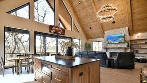 A spacious living area with a large island, wooden ceiling, and a stone fireplace. - Modern Cabin, Cozy and Peaceful (Lake Geneva)