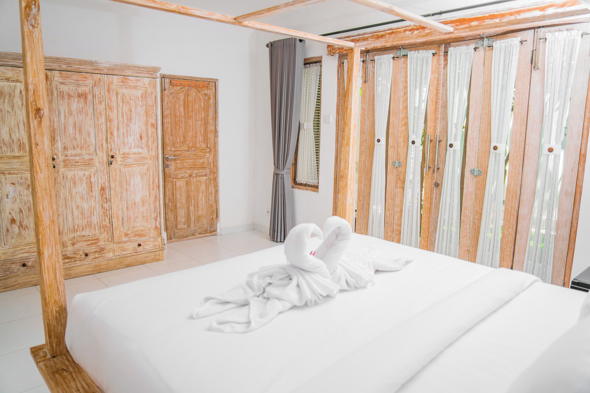 A hotel room with a large bed, wooden wardrobe, and curtains.