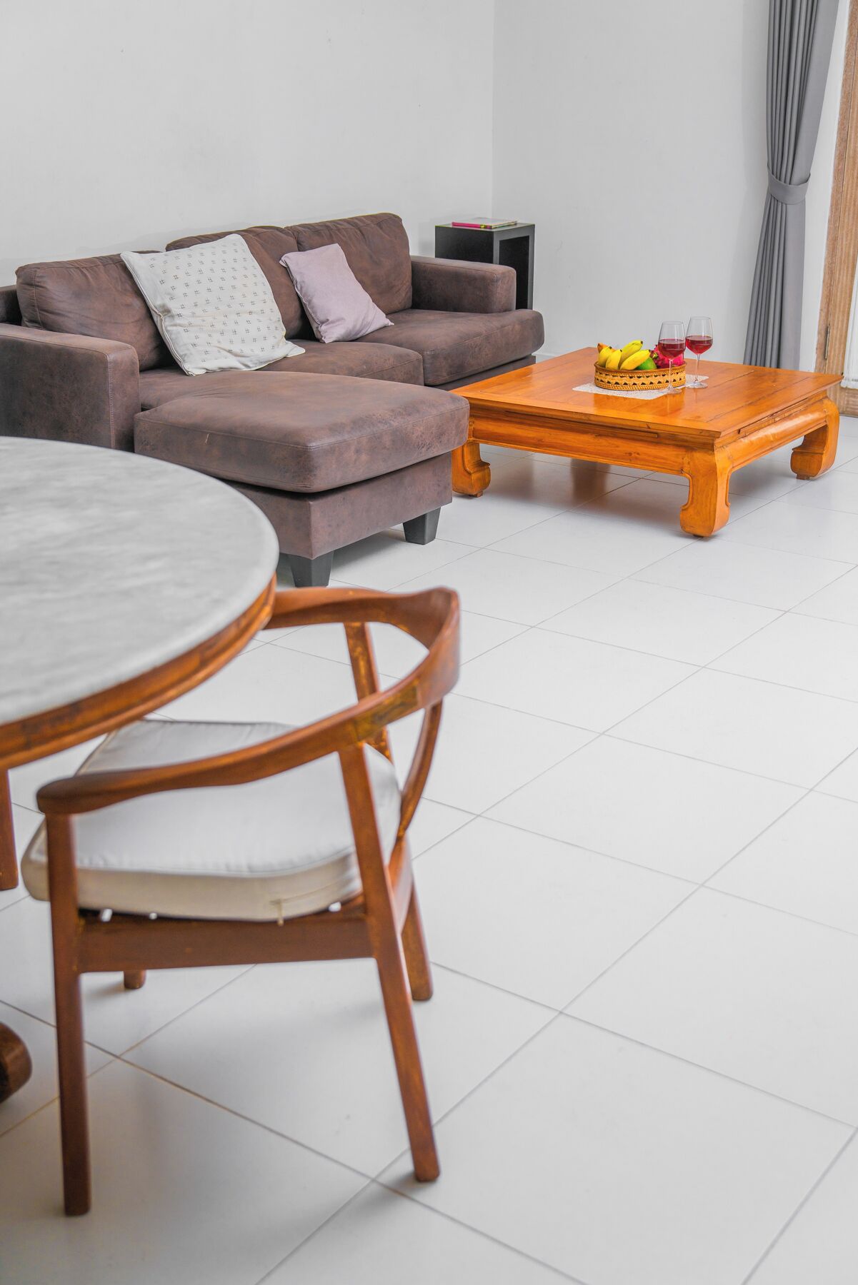 A living room with a brown sofa, a wooden coffee table with fruits and glasses, and a round table with chairs.