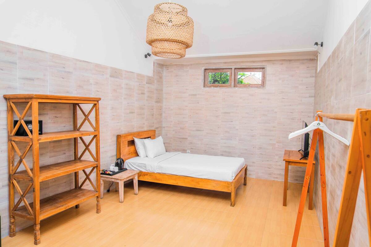 A room with a wooden bed, a wooden shelf unit, a small table, and a hanging light fixture.