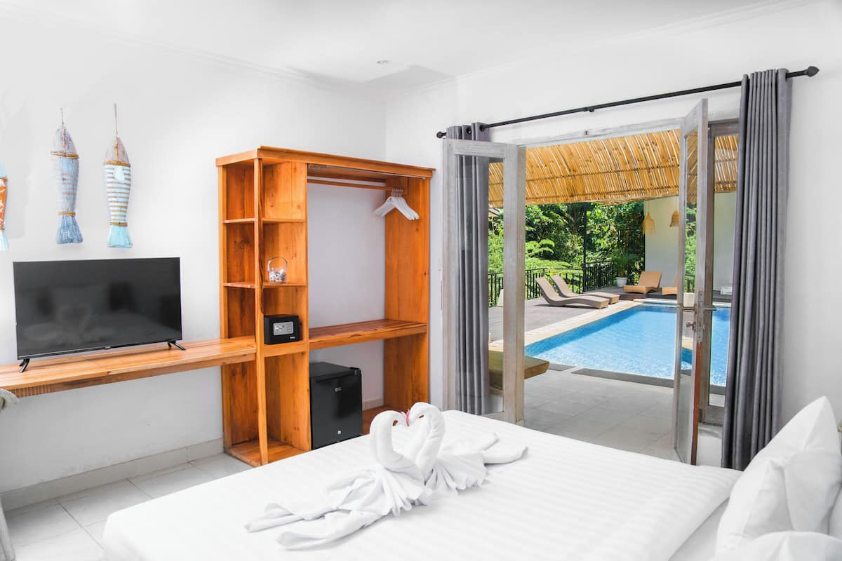 A hotel room with a bed, a TV, a wooden shelf, and a view of an outdoor swimming pool.