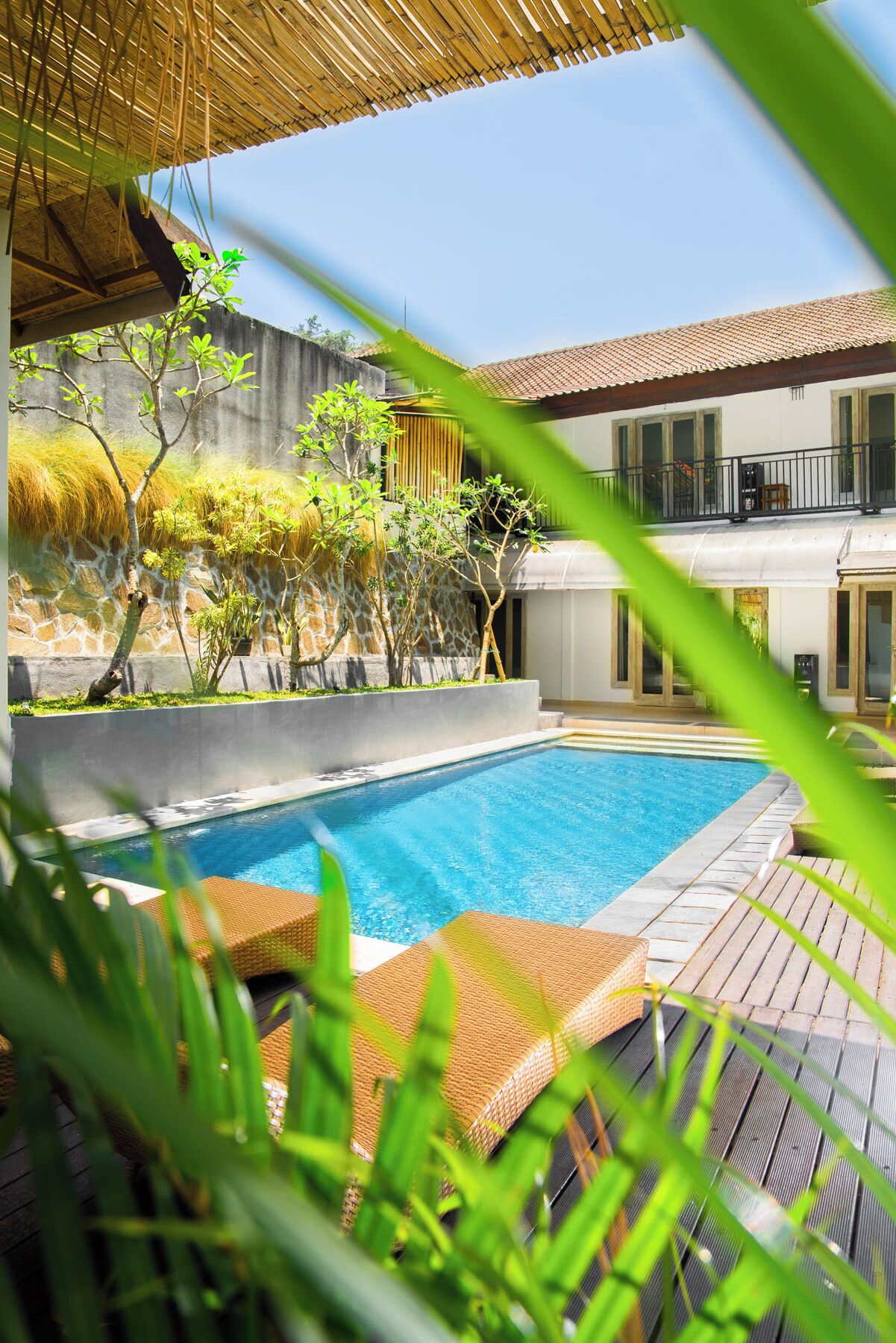 A swimming pool with a wooden deck, surrounded by greenery and a stone wall.