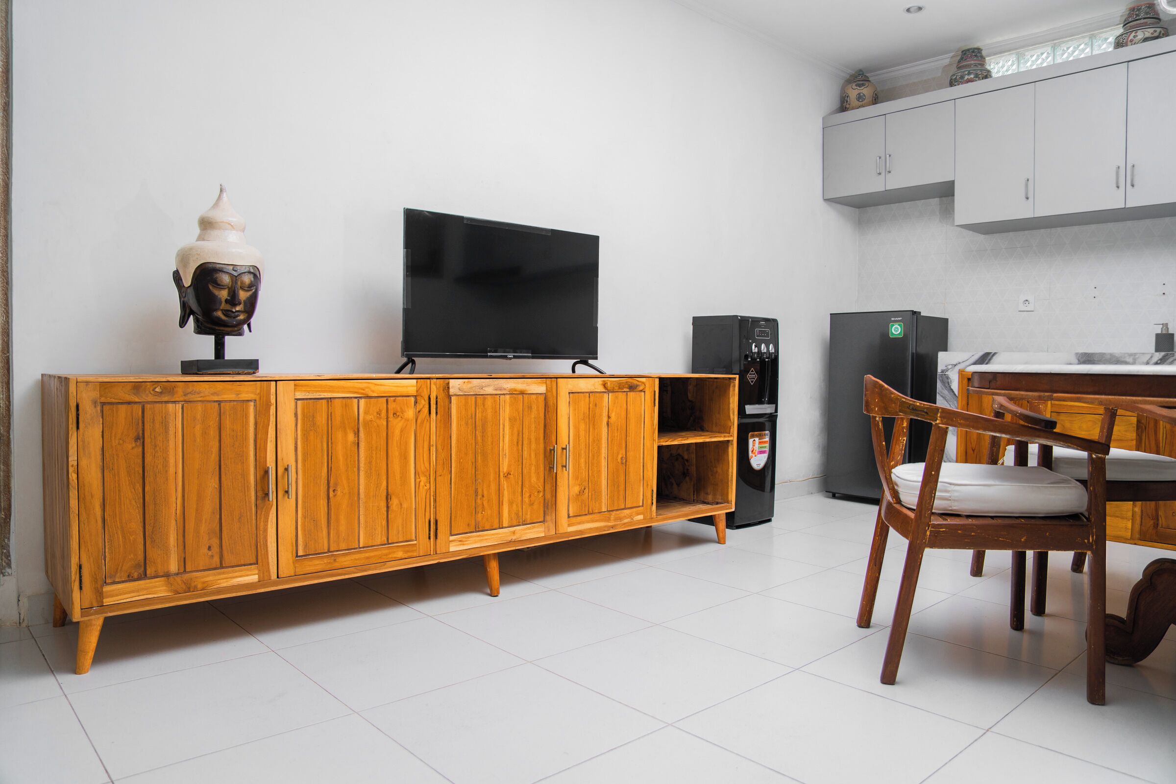 A wooden cabinet with a flat-screen TV, a refrigerator, and a dining table with chairs.