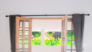 A room with a wooden door leading to an outdoor area, a bed, and a view of greenery. - Bali Invest Living (Tumbak Bayuh)