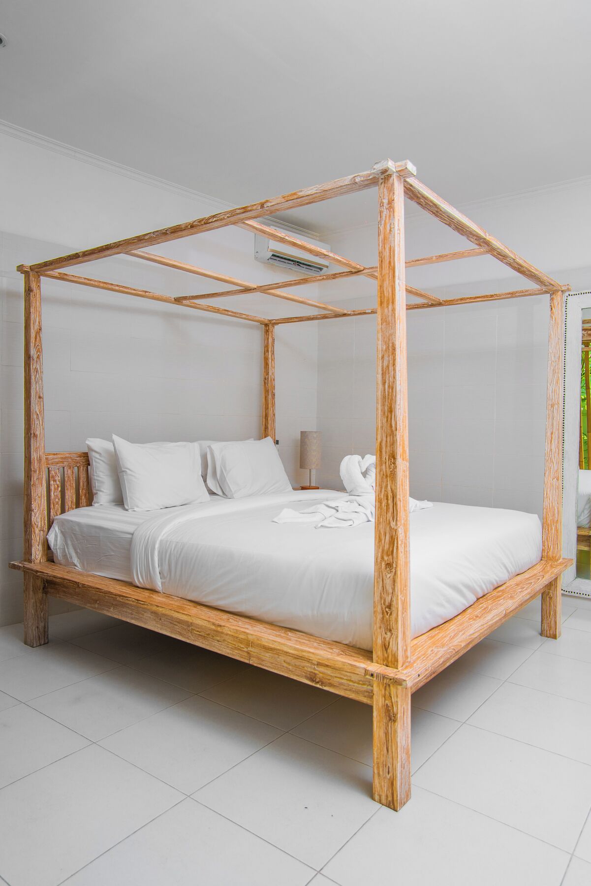 A four-poster bed with a wooden frame and white bedding in a room with white tiled flooring.