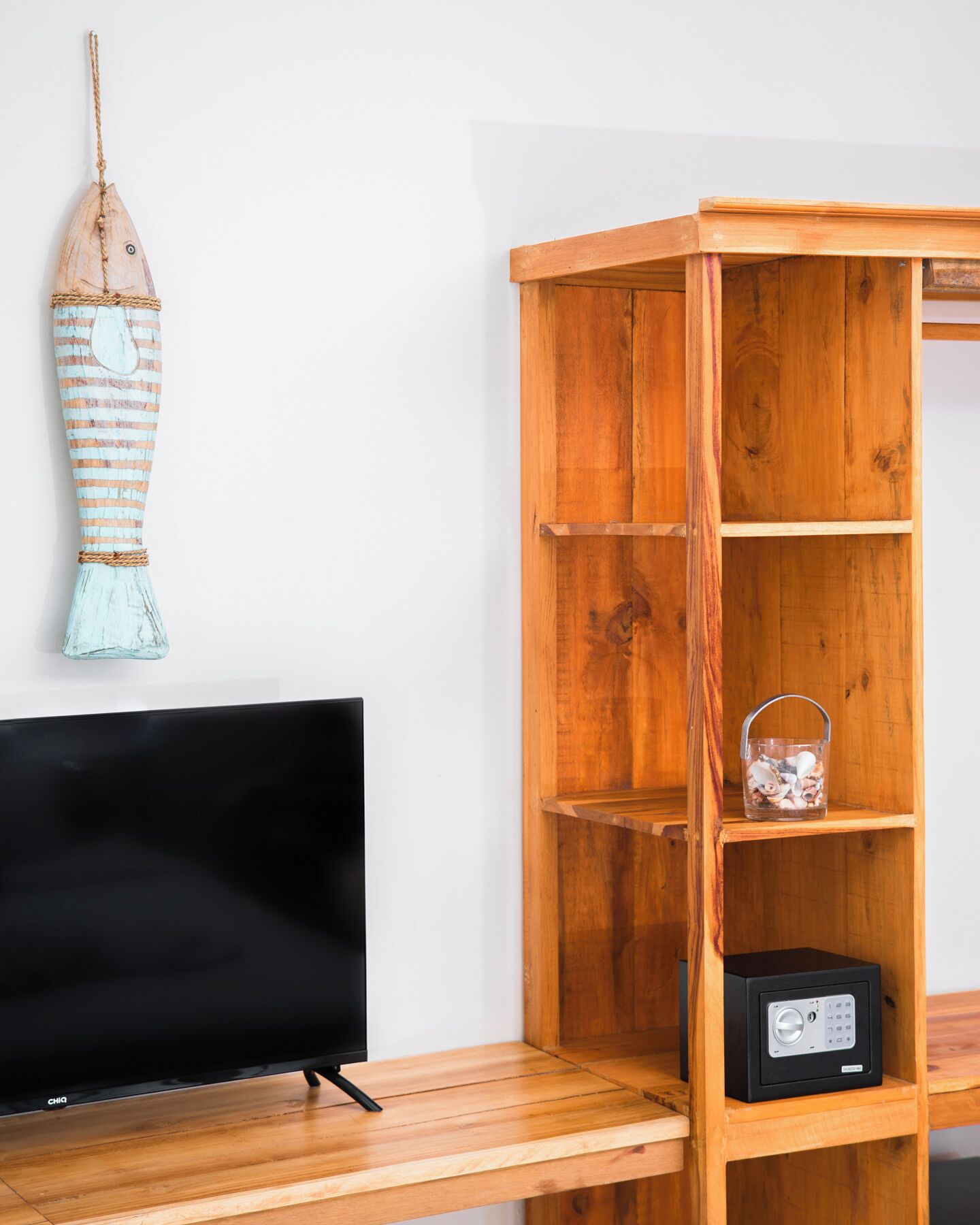 Een houten tv-meubel met een flatscreen televisie, een houten kast met planken en een decoratief hangend object.