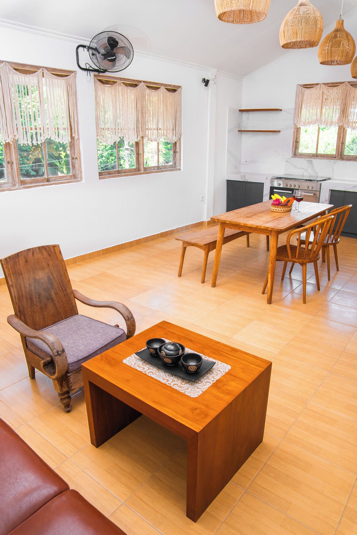 Un grand espace de vie comprenant une table à manger en bois, une chaise en bois et un canapé. Il y a également un coin cuisine avec une cuisinière et un ventilateur.