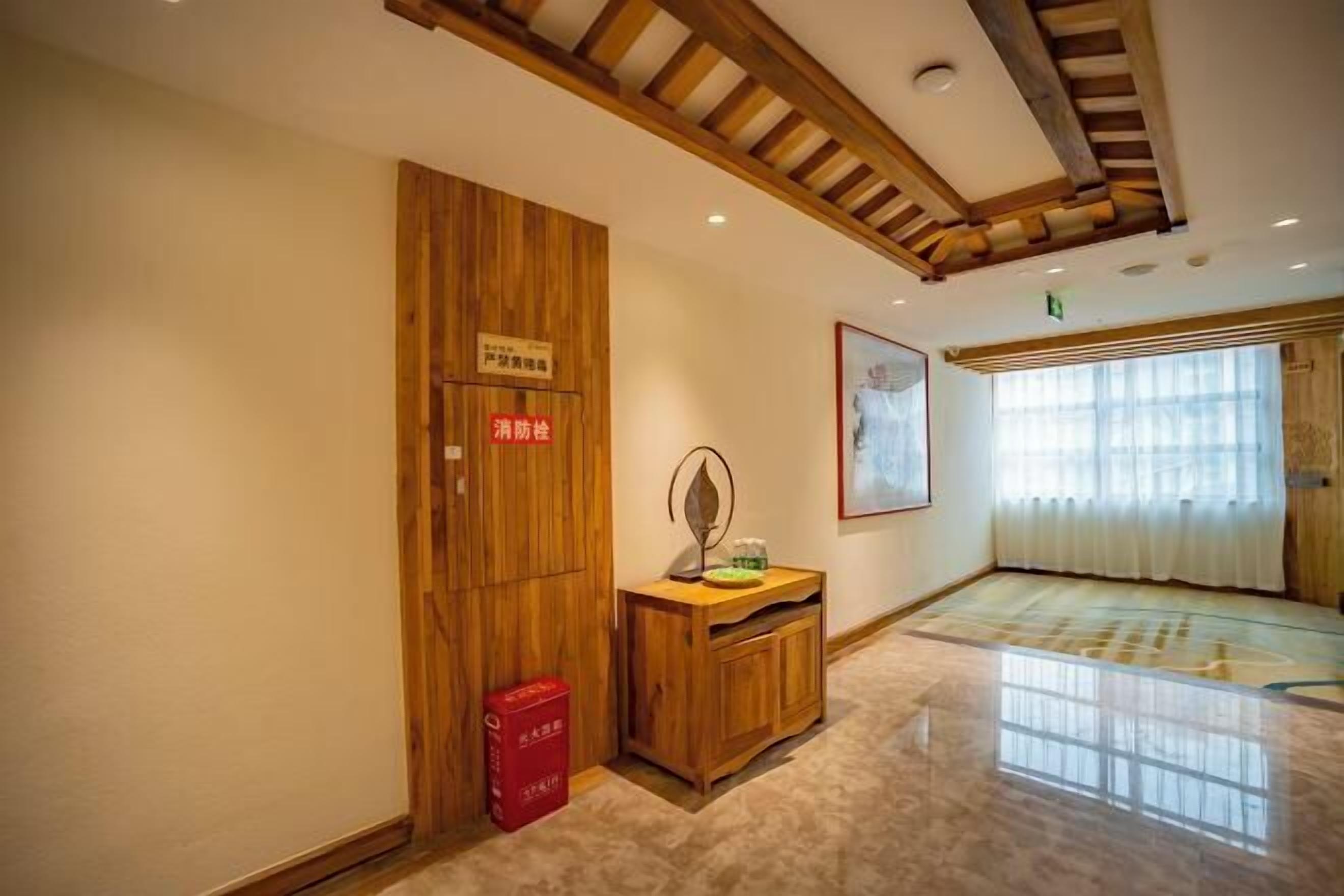 Habitación de hotel con paneles de madera, un armario de madera, un cubo de basura rojo y un ventanal con cortinas.