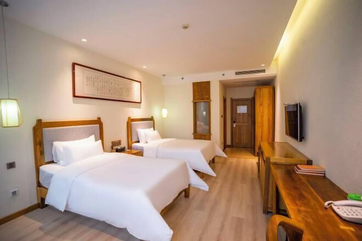 A hotel room with two beds, a desk, a TV, and a framed picture on the wall.