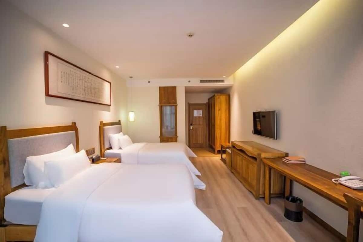 A hotel room with two beds, a desk, a TV, and a framed picture on the wall.