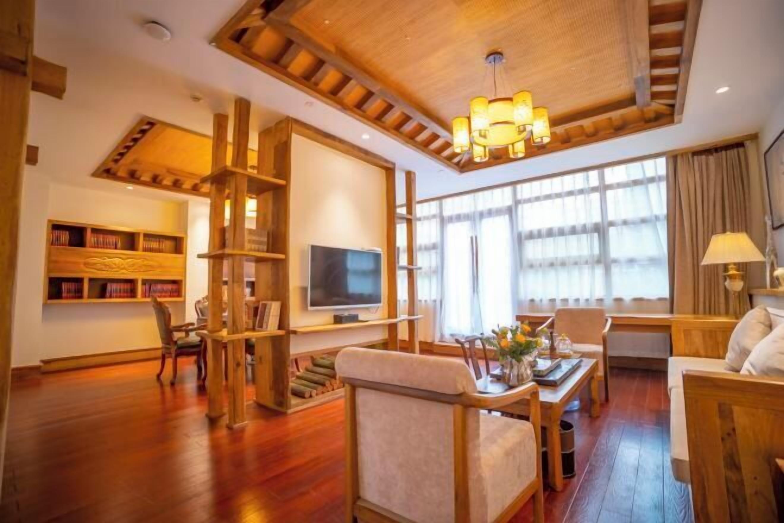 A spacious living area with a wooden ceiling, a television, a bookshelf, and a dining table with chairs.