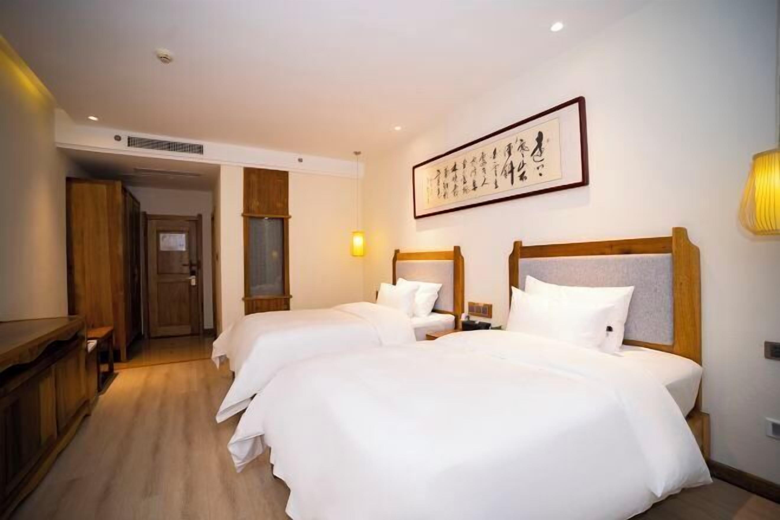 A hotel room with two beds, a wooden desk, and a framed artwork on the wall.