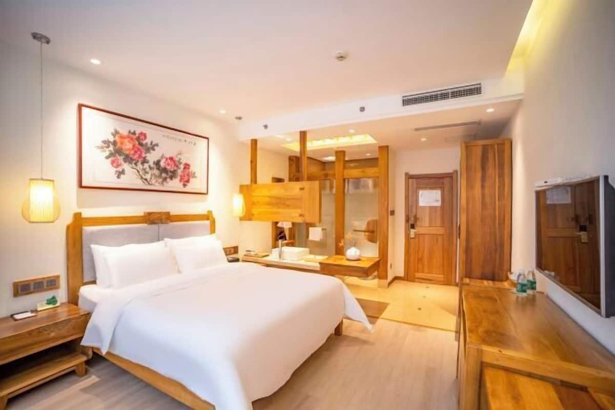 A hotel room with a large bed, bedside table, mirror, wooden wardrobe, and a television.