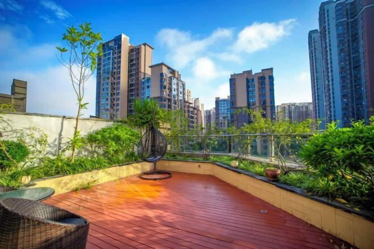 A rooftop terrace with a wooden deck, a hanging chair, and potted plants.