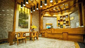 A wooden reception desk with a computer and a small plant. There is a painting on the wall and a wooden table with chairs. - Shuhanyuan Hotel Mianyang (Mianyang)