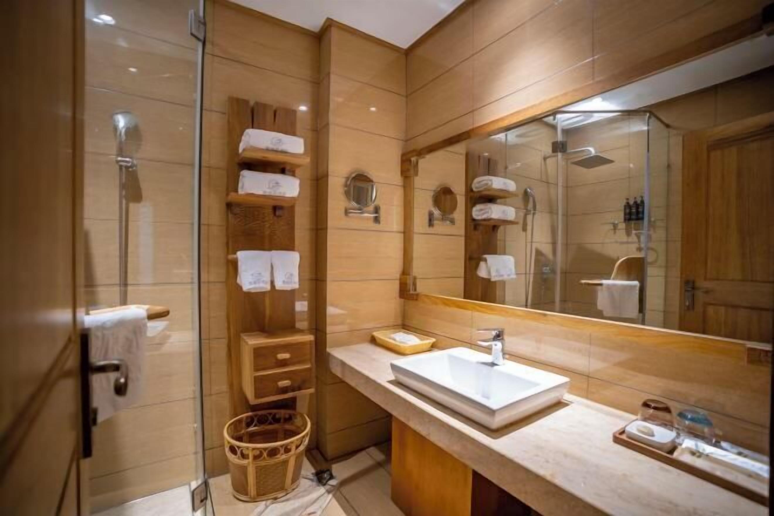 Uma casa de banho moderna com cabine de duche em vidro, toucador de madeira com um espelho grande e toalhas bem organizadas.