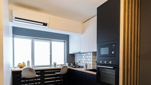 Eine moderne Küche mit integriertem Mikrowellenherd, Backofen und einem Fenster über der Spüle. Im Wohnbereich befinden sich zwei Barhocker und ein blaues Sofa.