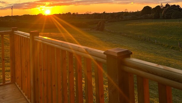 Una terraza de madera con vistas a una puesta de sol sobre un campo cubierto de hierba.