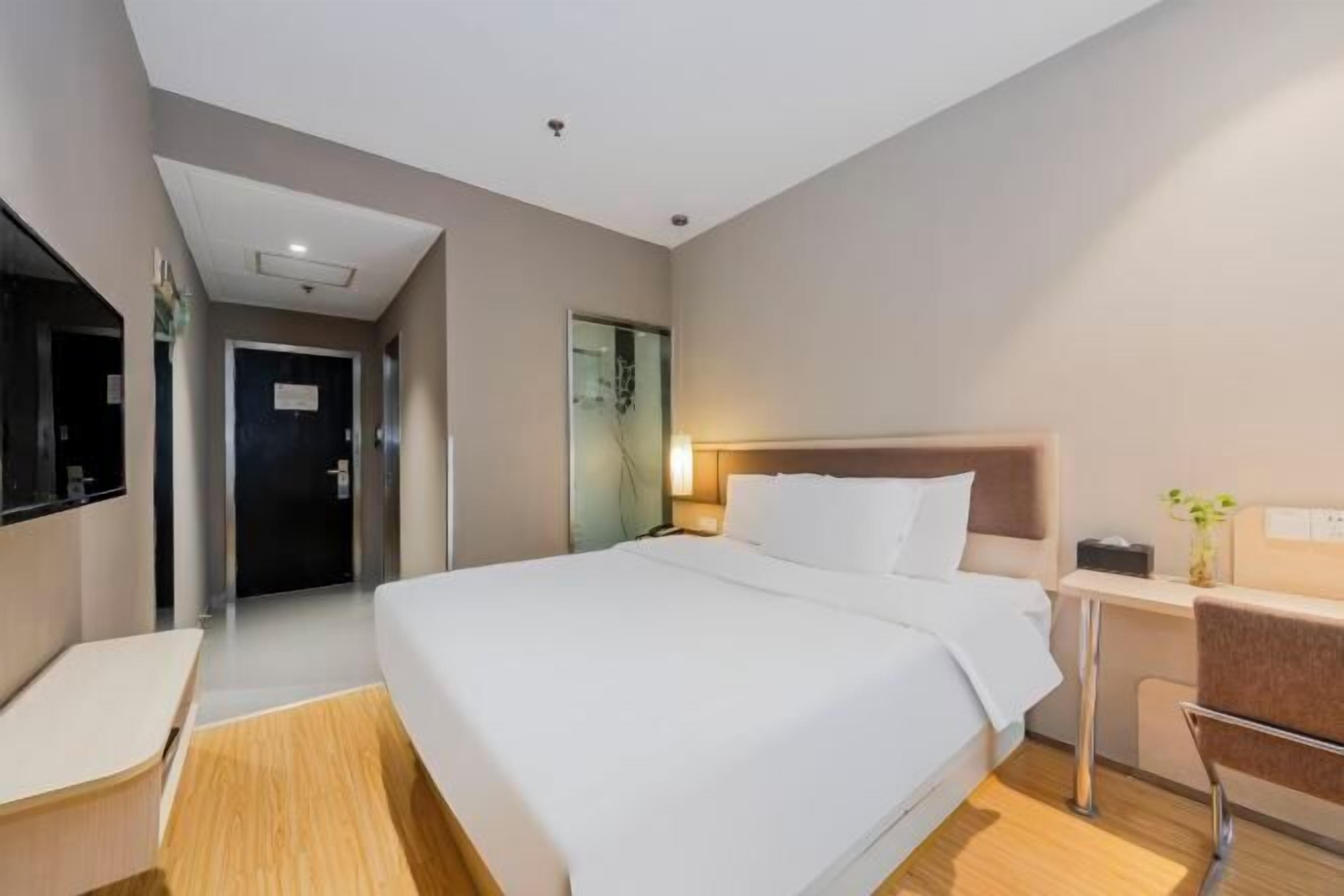 A modern hotel room with a large bed, a desk, a chair, and a television.