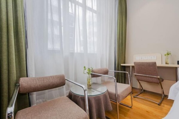 A hotel room with a bed, a round glass table with chairs, a small table with a vase, and a window with sheer curtains. - Homeinn Motel Hotel (Nanjing Medical University Longmian Avenue Subway Station) (Nanjing)