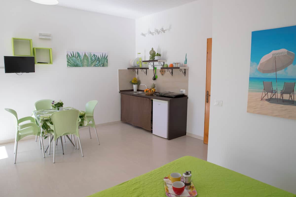 A modern kitchen with a dining area, a small refrigerator, and a painting of a beach scene.
