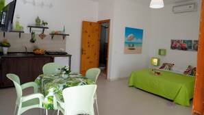 A compact room with a dining area, kitchenette, and a bed with a green bedspread. - Villa Maria (San Vito Lo Capo)