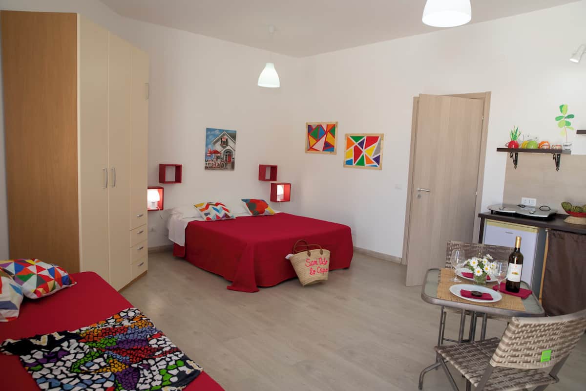 A bedroom with a bed, a wardrobe, a desk with a chair, and a dining table with a chair.