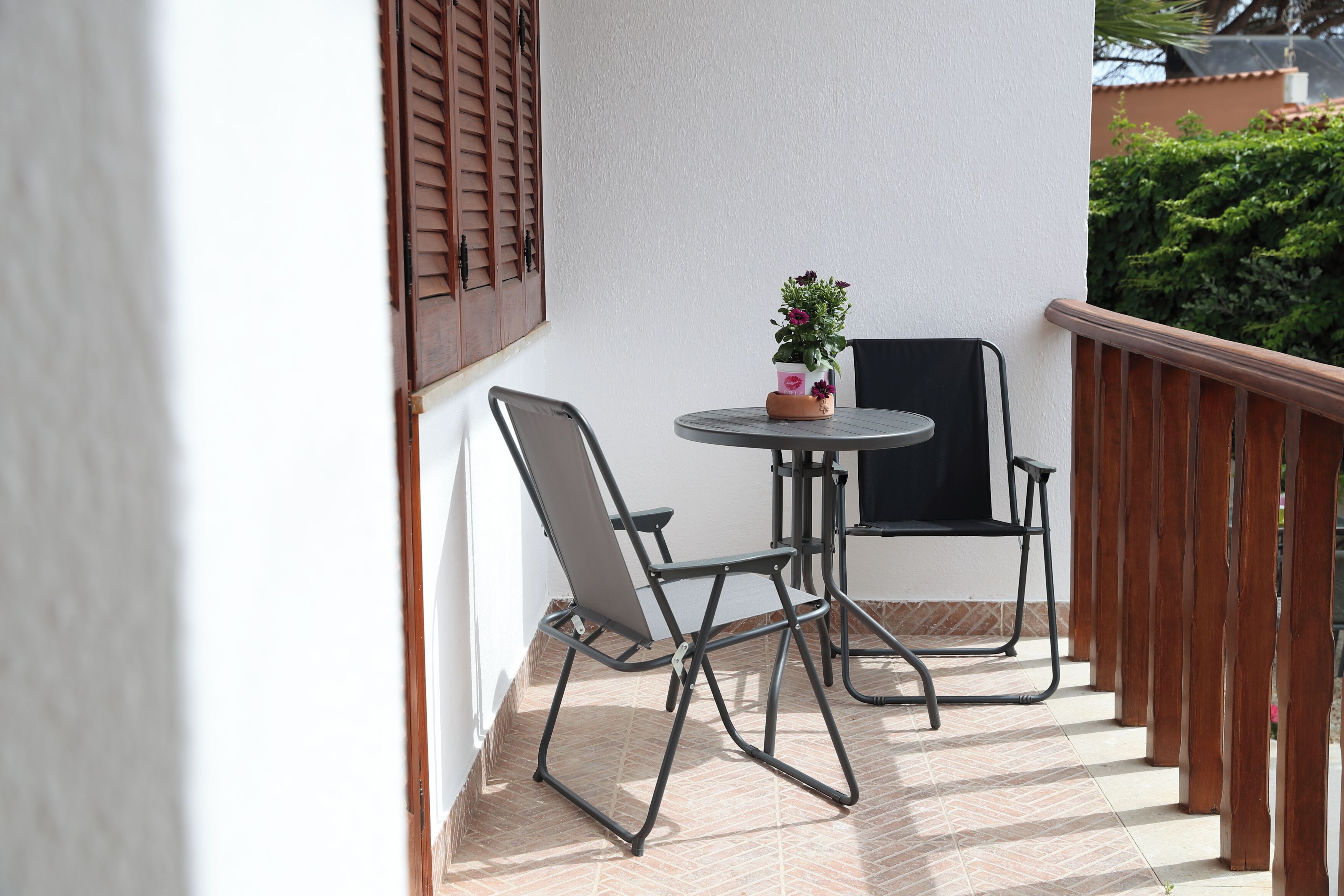 Un balcon avec deux chaises en métal, une petite table ronde et un pot de fleurs.