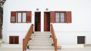 A staircase leading to a white building with wooden shutters and doors, potted plants at the base, and a small basket on the landing. - Villa Maria (San Vito Lo Capo)