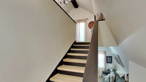 Un escalier avec des marches en bois et des rampes noires, menant à une pièce où se trouvent un canapé vert et une lampe blanche.
