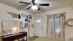 Une chambre à coucher comprenant un lit, une coiffeuse avec un miroir, un ventilateur de plafond et divers éléments de décoration murale.