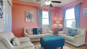 A living room with two sofas, a coffee table, a ceiling fan, and a window with curtains. - Twin Palms at Surfside by Ryson Vacation Rentals (Freeport)